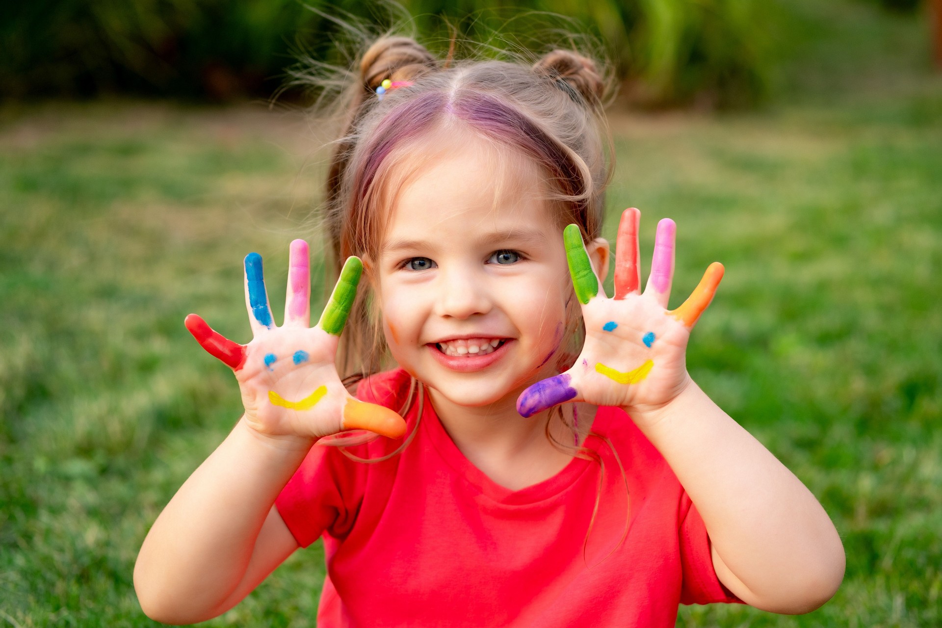 a small child girl with painted fingers in bright colors on her hands in summer on a green lawn, a bright summer photo of a happy child with colorful fingers in colors